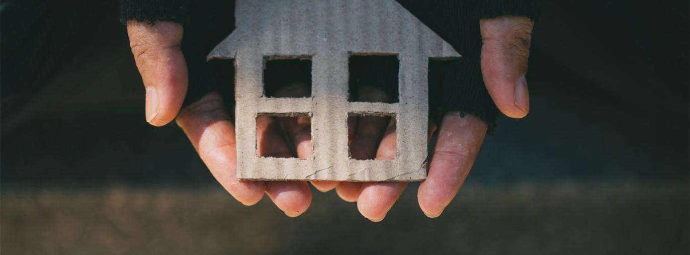 photo de mains avec des gants abimés portant une maison en carton