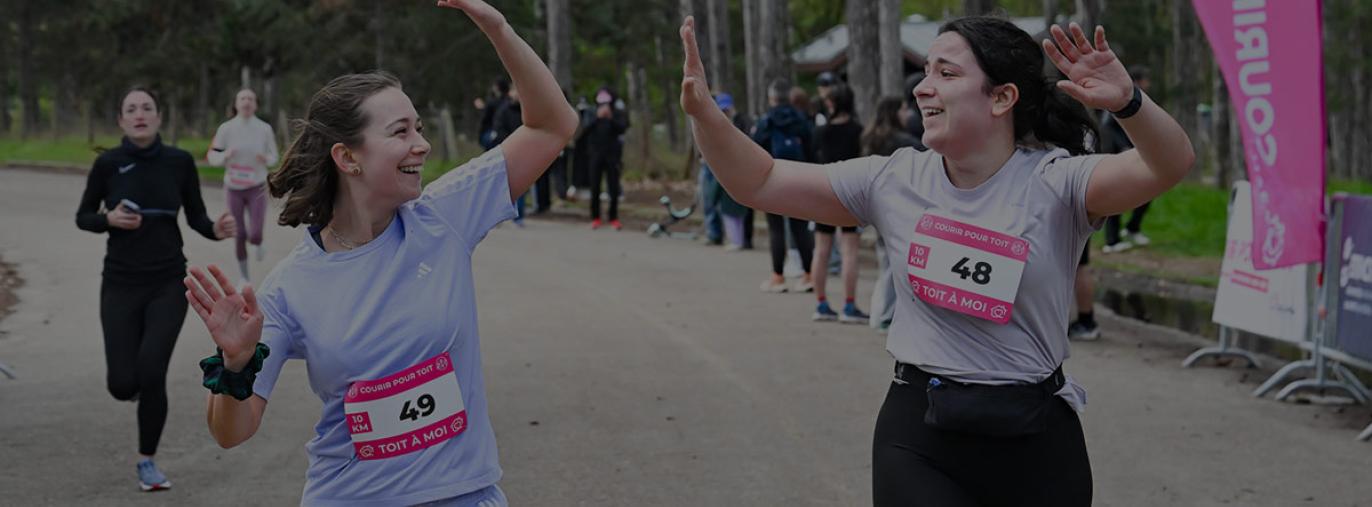 Deux coureuses se tapent dans les mains sur la ligne d'arrivée du 10 km de la course courir pour toit
