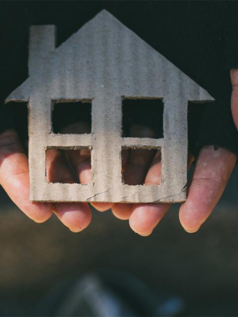 photo de mains avec des gants abimés portant une maison en carton
